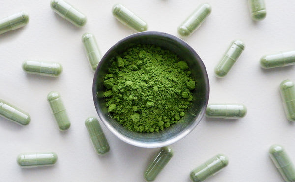 A bowl of matcha tea powder surrounded by small, green matcha supplements.