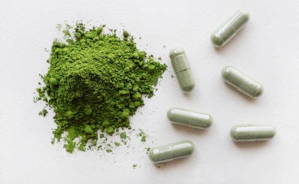A pile of matcha powder surrounded by green matcha supplement pill capsules.

