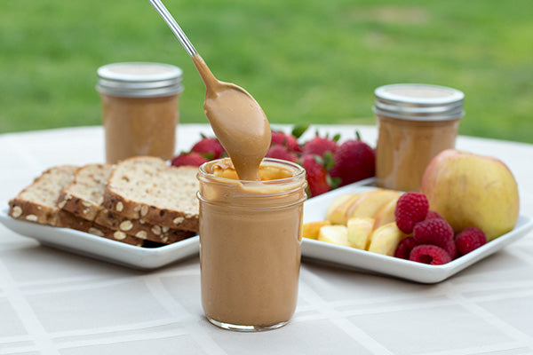 Spoonful of Coconut Peanut Butter out of jar with fruit and bread - Aloha Spreads