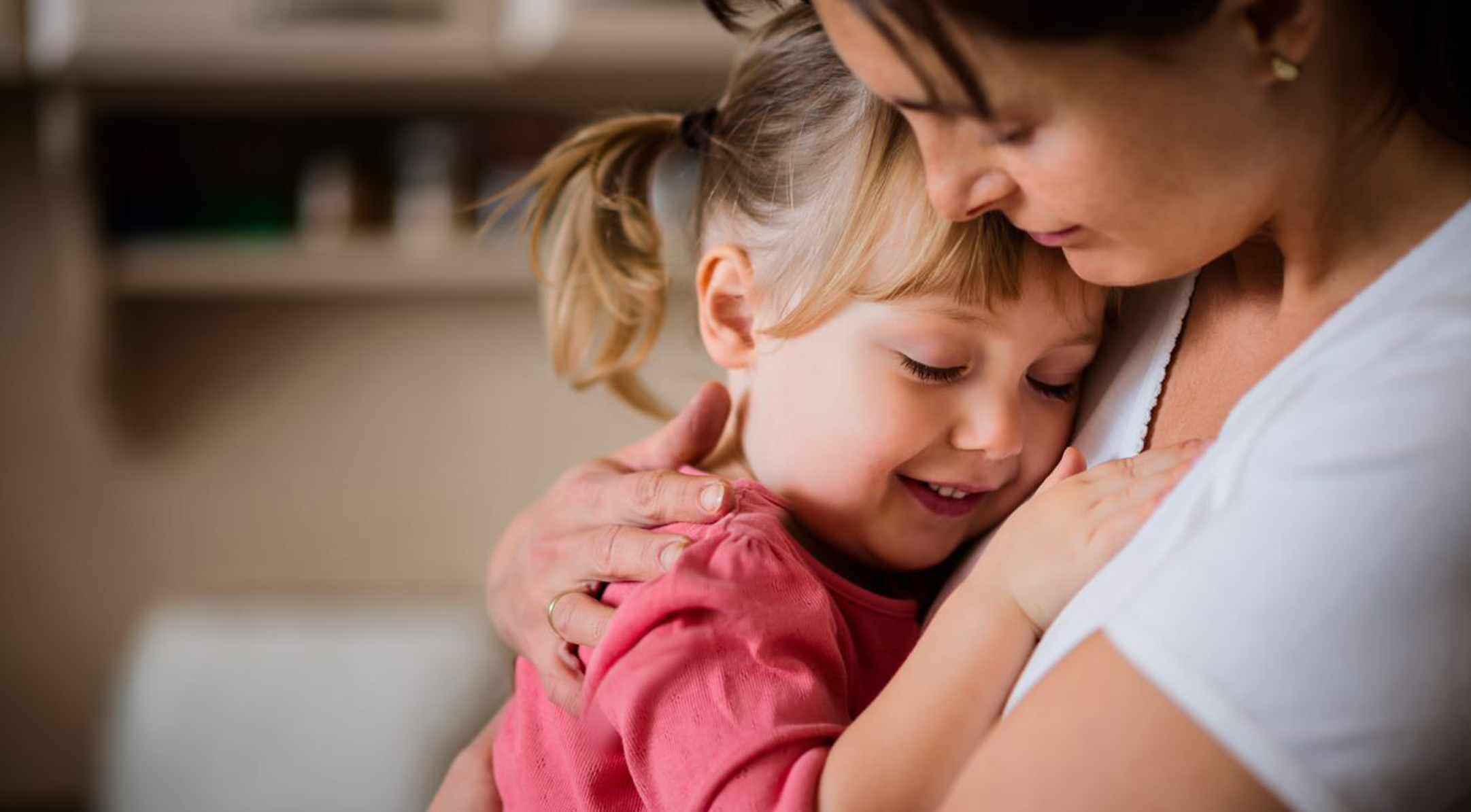 Mother hugging daughter against chest smiling
