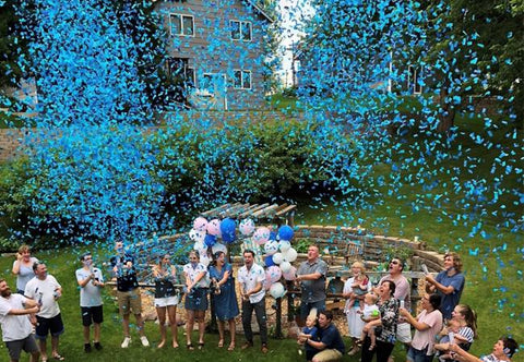 Gender reveal party shooting blue confetti cannons to celebrate the couple having a boy.