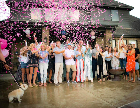 Family and friends shooting confetti cannons exposing pink confetti in celebration of the couple having a girl.