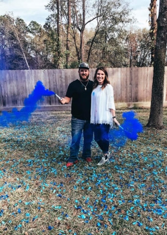 Couple posing with blue smoke to announce them having a baby boy.