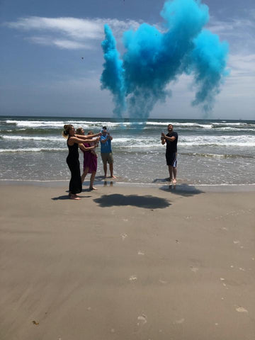 Family celebrating having a baby boy with a blue smoke cannon on the beach.