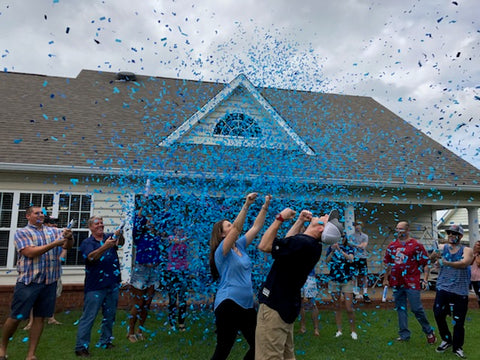 Couple celebrating the gender of their baby with family and friends, by shooting blue confetti.
