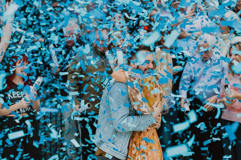 Couple hugging while being covered in blue confetti, celebrating having a baby boy.