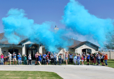 Couple surrounded by family and friends outside with blue smoke in the air.