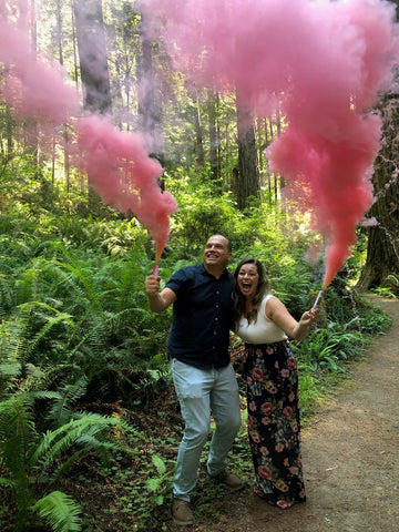 Couple posed in a forest with pink smoke cannons.