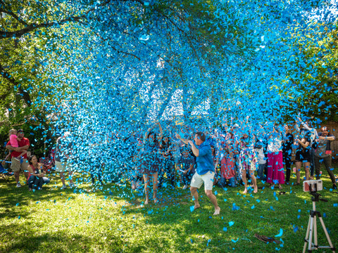 Family and friends shooting confetti cannons exposing blue confetti. Celebrating the couple having a boy.