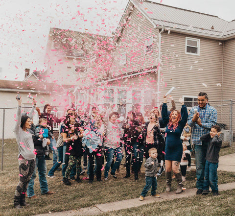 Friends and family surrounding a couple outside with pink confetti in the air.
