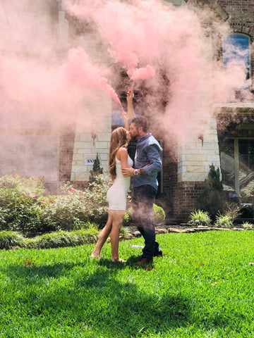 A couple posing with pink smoke bombs, announcing them having a baby girl