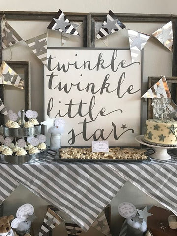 Table with grey decorations and grey colored sweets on it. With a sign that says "twinkle twinkle little star" on it.