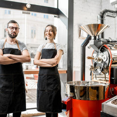 Two Roastery workers standing next to a Roaster