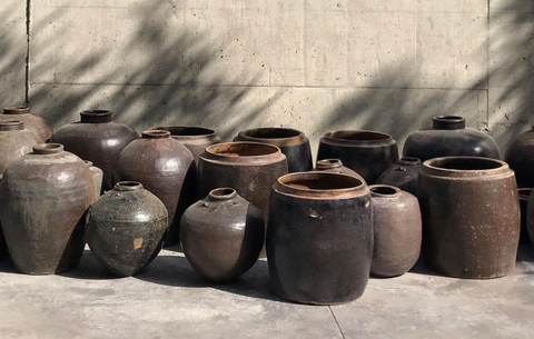 Collection of antique Chinese pots positioned in front of concrete wall.