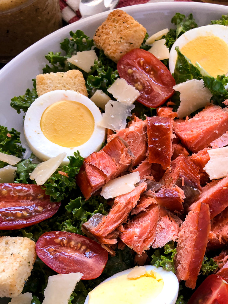 Close up of smoked salmon on a bed of greens with hardboiled eggs and tomatoes.
