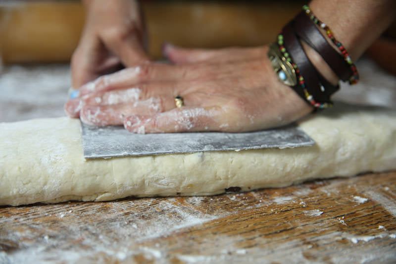 Gently press down the rolled up dough with the dough cutter in order to flatten the surface, creating a long rectangle.