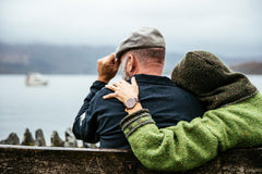 Photo of a man and woman with their backs to us, sitting on a bench looking out over the water.