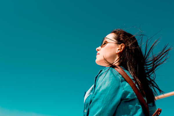woman in a denim jacket with dark hair blowing in the breeze under a blue sky