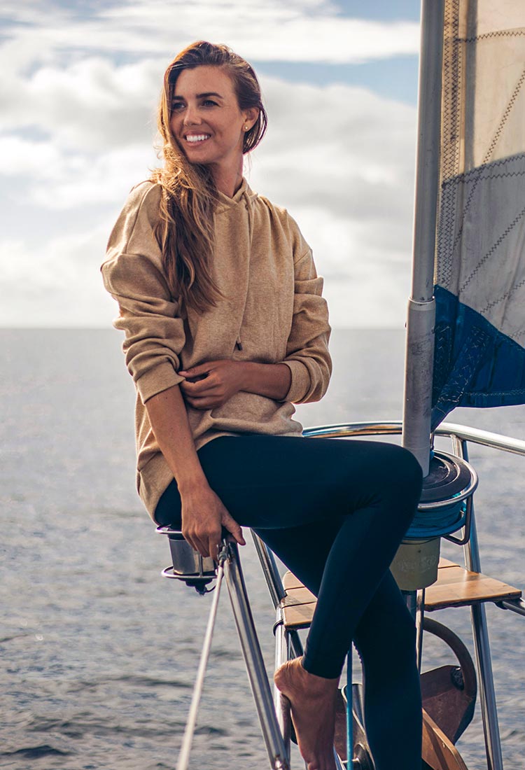 Rachel Moore sailing on her boat among blue skies, wearing a beige MPG hooded sweatshirt and blue leggings