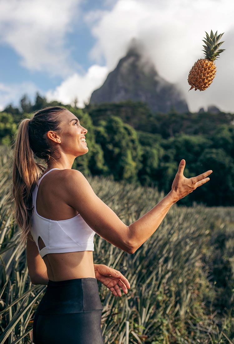 Rachel Moore tossing a pineapple in front of a breathtaking tropical mountain view