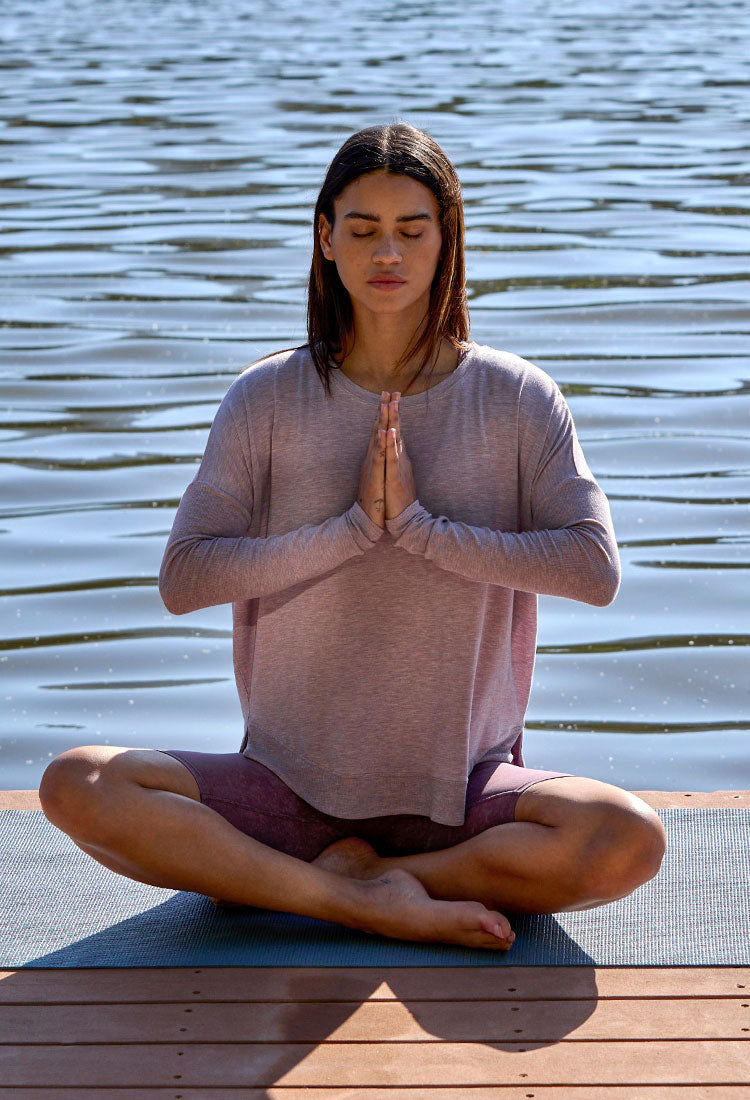 MPG female model meditating cross-legged on a dock by a lake