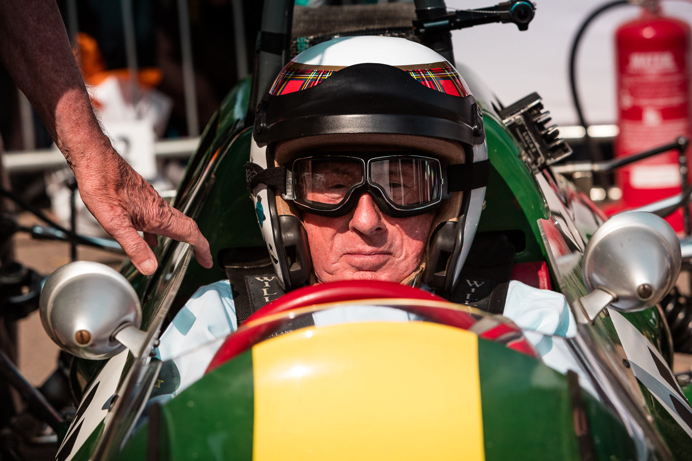 Sir Jackie Stewart is sitting in a 60s Lotus Formula 1 Grand Prix race car wearing a helmet and goggles. (Photo: Alex Lawrence – The White Wall 2018)