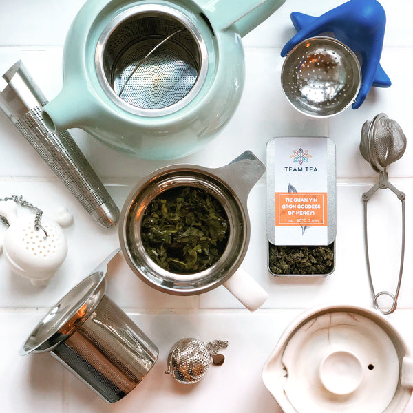 A collection of various tea strainers, sat with a tin of Team Tea's loose leaf tea. There are cup strainers, teapot strainers and a whole host of other types.