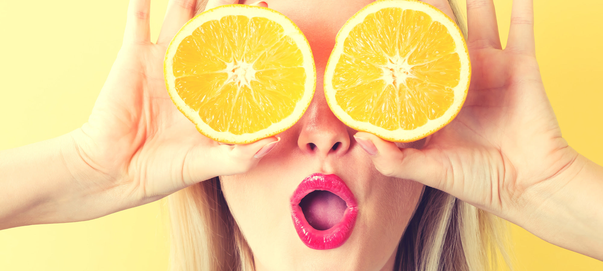 Woman holding orange slices over her eyes