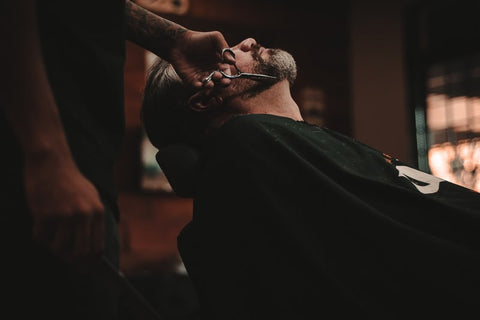 A man sitting back in a barber’s chair, getting his beard trimmed