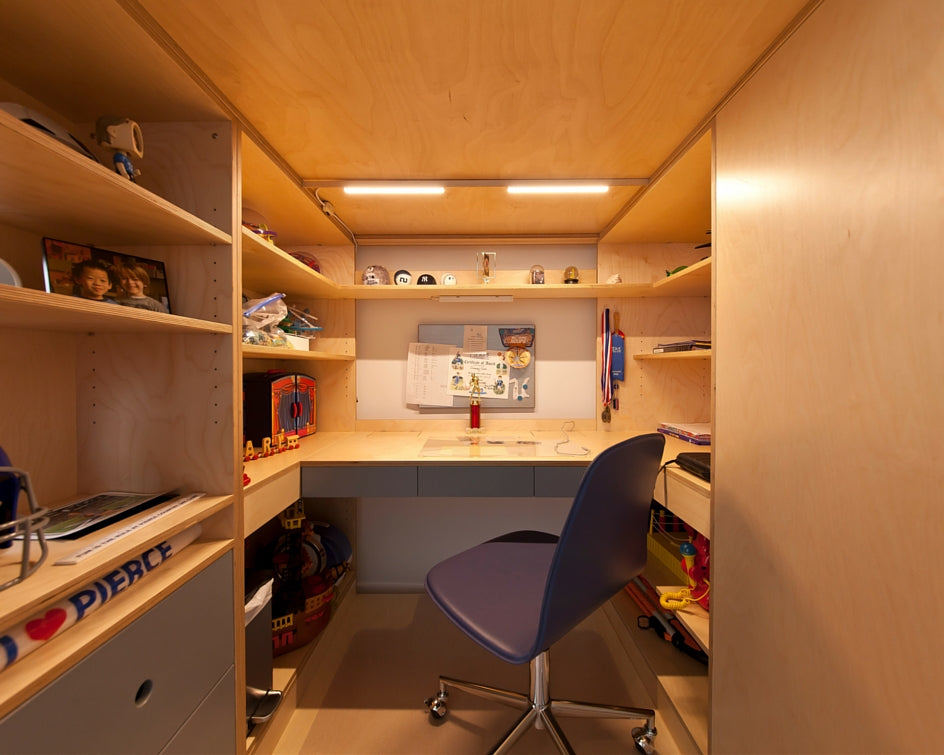 Compact home office nook with a desk, ergonomic chair, and shelves in a warmly lit wooden cubicle.