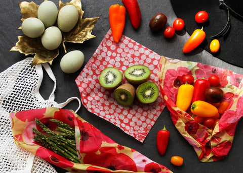 A spread of farmers' market goodies on a dark slate surface: blue tinted eggs, red orange and yellow sweet peppers, cut kiwis, and asparagus in various Z Wraps. A shopping bag and sun hat peek out from opposite corners.