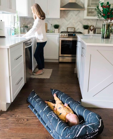 mother washing up at the sink whilst baby lies in DockATot