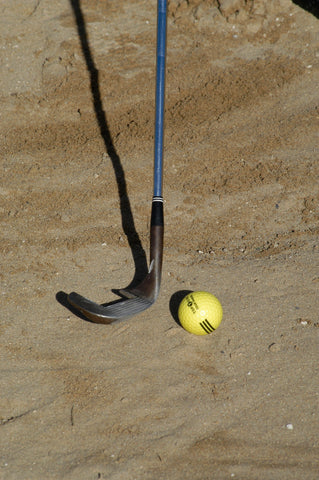 Golf club and yellow golf ball in sand