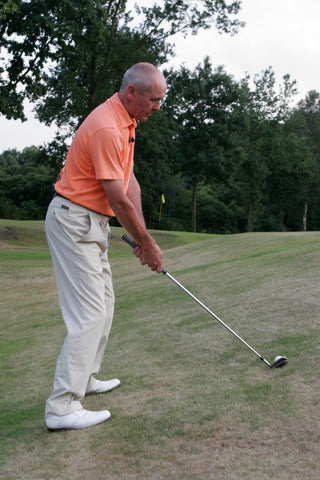 Keith Williams hitting a golf ball up the side of a small hill in an orange shirt.