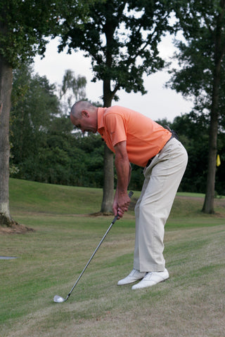 Keith Williams hitting a golf ball on the side of a hill in an orange shirt.