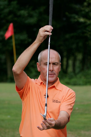 Keith Williams holding a golf club vertically in an orange shirt