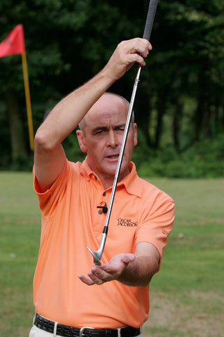Keith Williams holding a golf club leaning forwards in an orange shirt