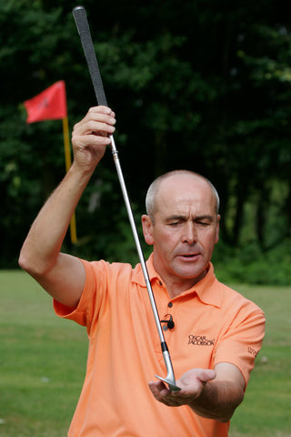 Keith Williams holding a golf club leaning backwards in an orange shirt