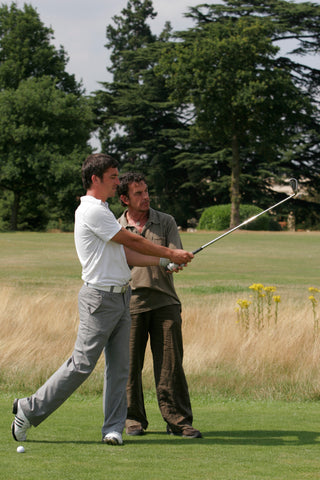 Steve Gould watching a man in white shirt practise with his golf club