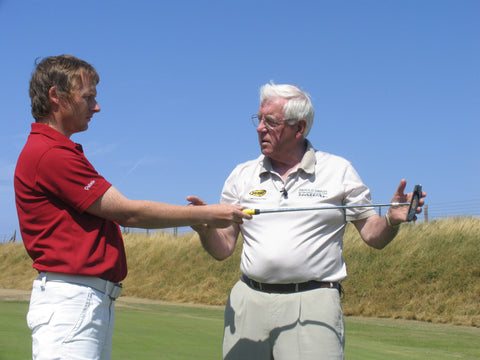 Harold swash talking to a man in a red shirt holding a golf club