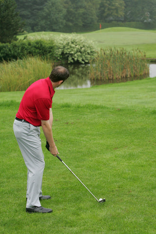 Karl Morris hitting a golf ball, over a pond in a red shirt.