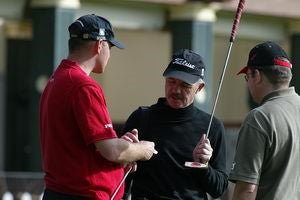 Thomas Bjorn in a black shirt with a golf club and talking to two men