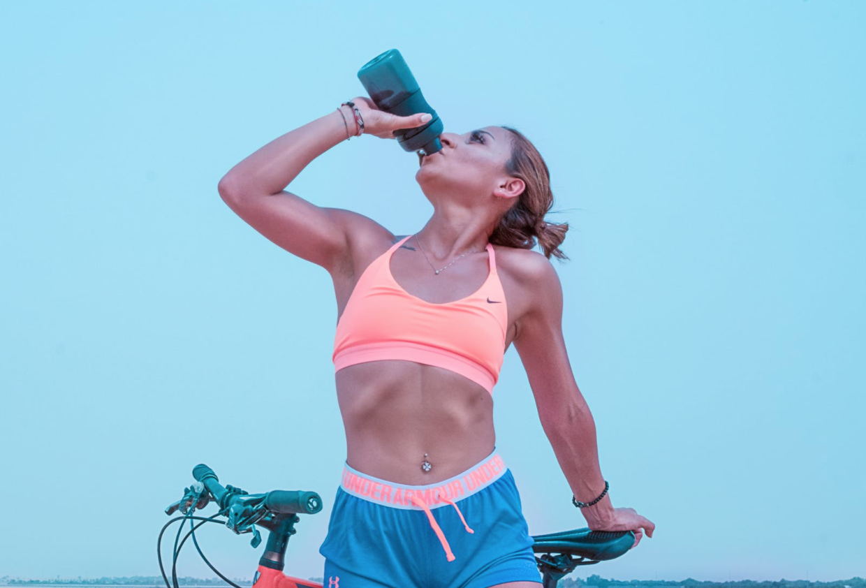 Female cyclist aware of whey protein powder side effects is drinking liquid collagen from her sports bottle