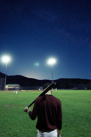 man facing baseball field with bat alone at night under the lights