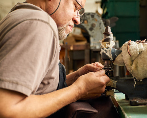 A middle aged african american man sits behind a machine carefully sewing luxury designer cork purses