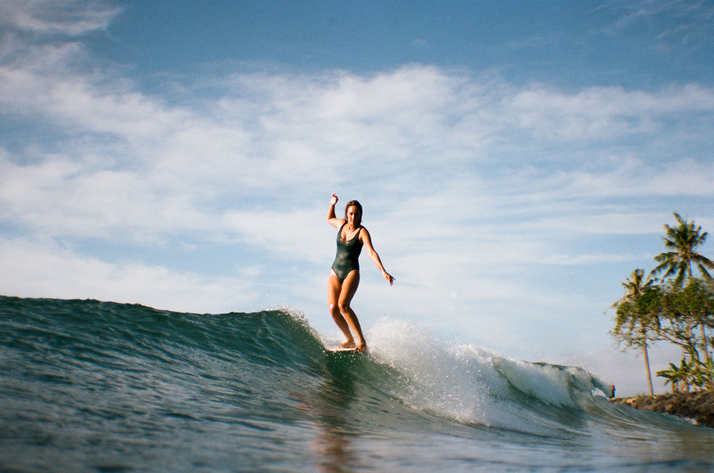 Sierra nose riding on her longboard, wearing a one piece surf swimsuit