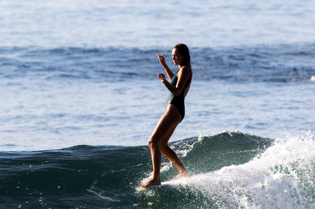 Sierra nose riding on her longboard, wearing a one piece surf swimsuit in Ivory