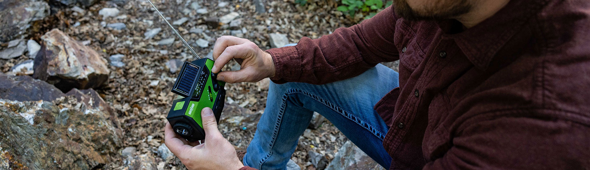 Male outdoor survivalist lost in the woods sitting at the edge of a lake, wearing a backpack filled with survival gear, looking at his tablet and searching for directions back to civilization.