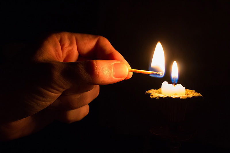 Man's handing lighting a candle in the dark
