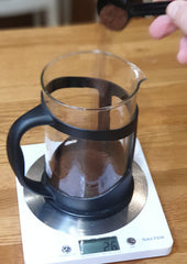 pouring ground coffee into a cafetiere which is sitting on kitchen scales